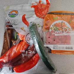 Pictured is a bag of peppers, a cucumber, and a container of cherry tomatoes.