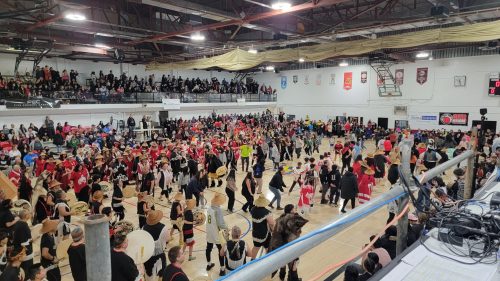 Large gathering of people dancing in the centre of a basketball court