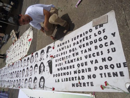una pancarta en el suelo con muchos rostros y un hombre mira la pancarta