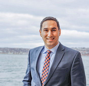 Portrait photo of Michael Kabalen. He is wearing a suit and there is an ocean behind him with a shoreline.