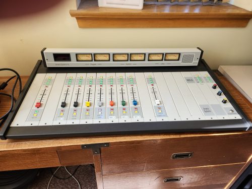 An audio mixing console sits on a desk