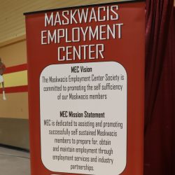 A tall poster for the Maskwacis Employment Centre at a conference, explaining who they are, and their mission. The photo was taken inside a gymnasium, where the conference was taking place.