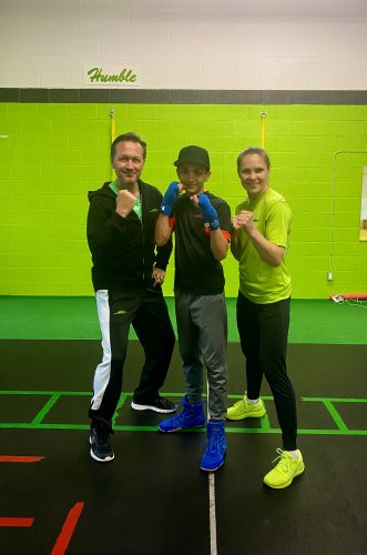 DiNola stands in Blaze Performance Training, a bright-green painted room. He's in a fighting stance posing with two trainers. 