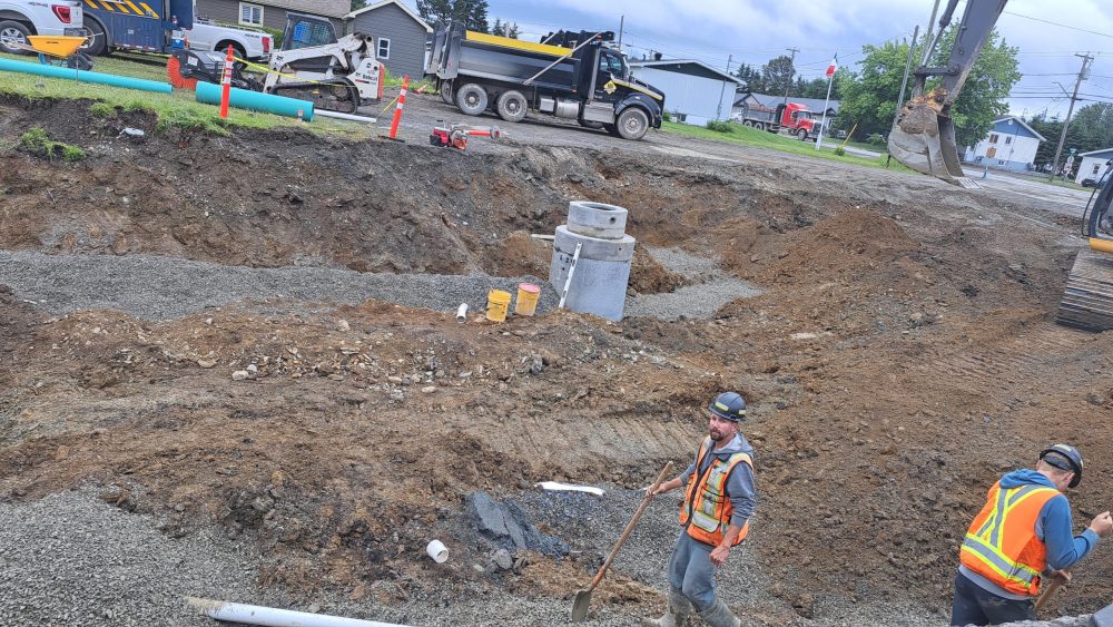 Deux hommes de la construction en dossard orange, sur le chantier des travaux de la rue Notre-Dame à Kedgwick, lors d'une journée d'été nuageuse.