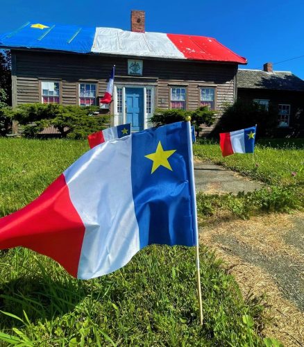 Des drapeaux acadiens en avant d'une vieille maison.