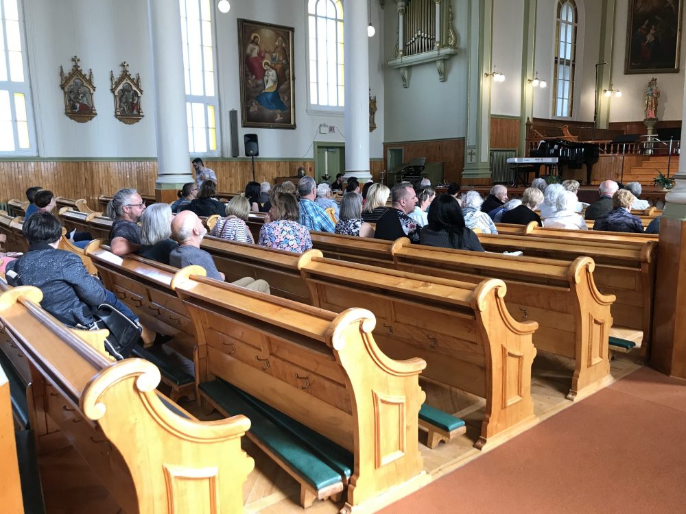 Des gens assis sur des bancs d'église, attentif à ce qui se déroule sur la scène