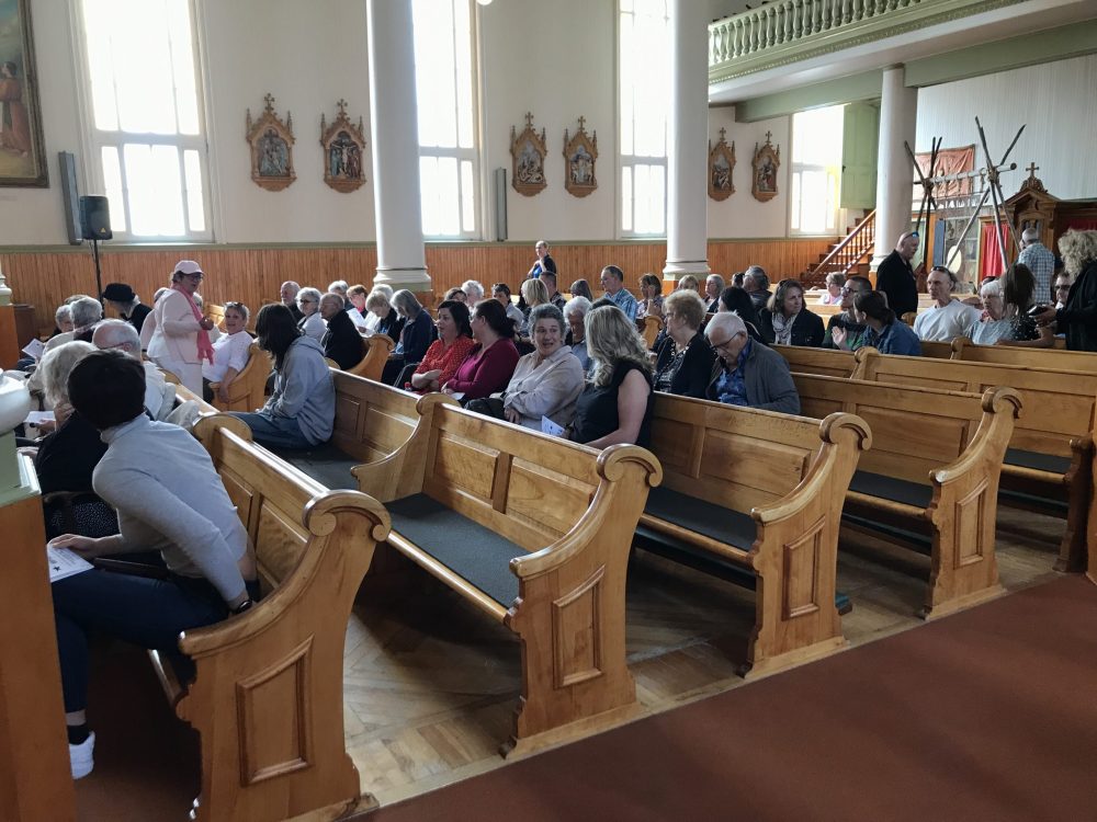 Des gens assis sur des bancs d'église, attentif à ce qui se déroule sur la scène