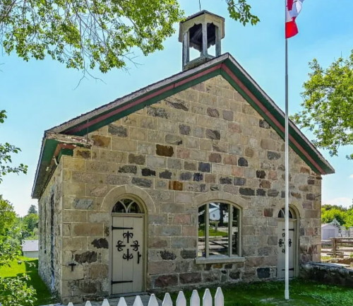 A sunny day at Belwood's Skol house, an old-time school house with a Canadian flag with green grass.