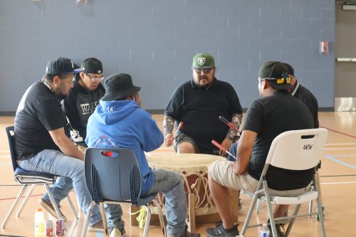A drum circle happens during the treaty commemoration. The photo was taken near a window in a gymnasium.