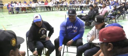 In a gymnasium of onlookers, a ceremonial drum circle takes place with Blue Jays alumni Jesse Barfield partaking in the circle.
