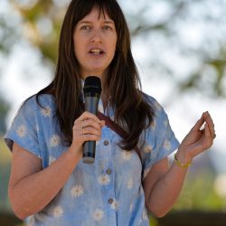 Woman wearing a light blue shirt speaks into a microphone