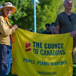 Two protesters hold a yellow Council of Canadians banner.