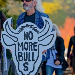 Man holding a sign reading No More Bull S shaped like a bull's head.
