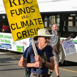 Man holding a sign reading RBC funds the climate crisis