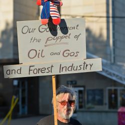 Man holds a sign reading our government is the puppet of oil and gas