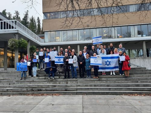A crowd is assembled at the top of Prince George City Hall's steps. Standing centre is Sean Farrell with the city's mayor. Flags of Israel and Canada can be seen.