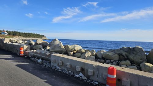 A concrete retaining wall has fallen into armour rock along the seashore