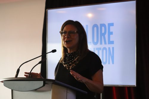 Traci Bednard, the CEO of Explore Edmonton, stands at a podium making hand gestures during her speech. The "Explore Edmonton" logo is behind her on a screen.