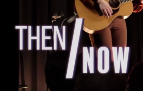 Bold white Helvetica font reads "Then/Now" In the background Prince George Performer Genevieve Jaide holds a guitar, her hand and pants are visible, the stage curtain backdrop is to the right,