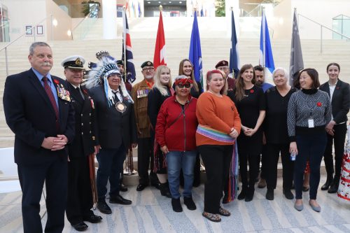 City councilors, veterans, dignitaries, and community members alike gather at Edmonton's City Hall to recognize Indigenous Veterans Day. Lots of colorful outfits and regalia is being worn. Photo was taken inside.