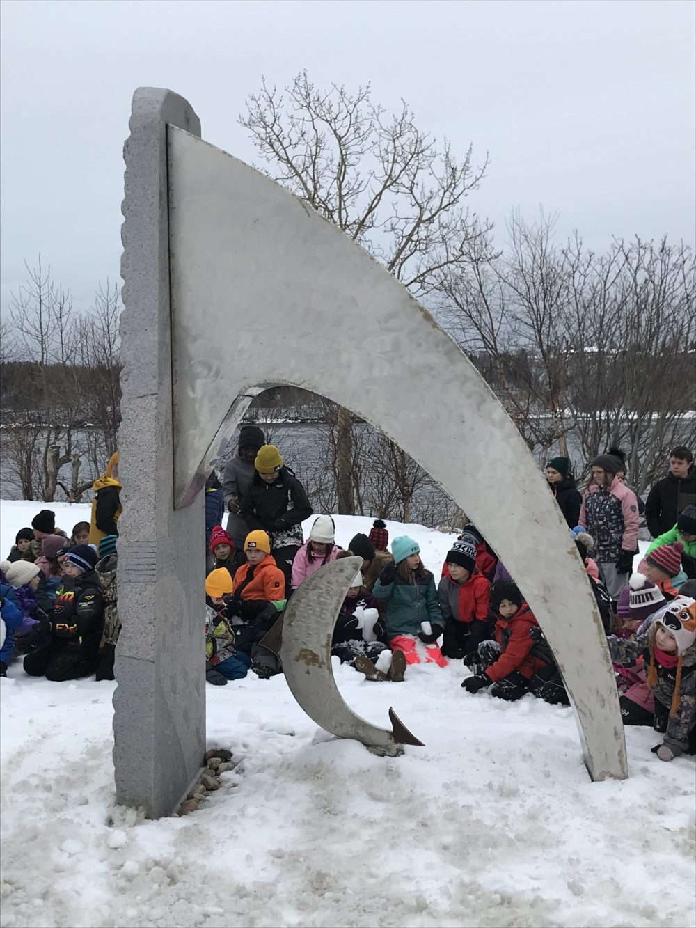 Des jeunes habillés en hiver près de la sculpture