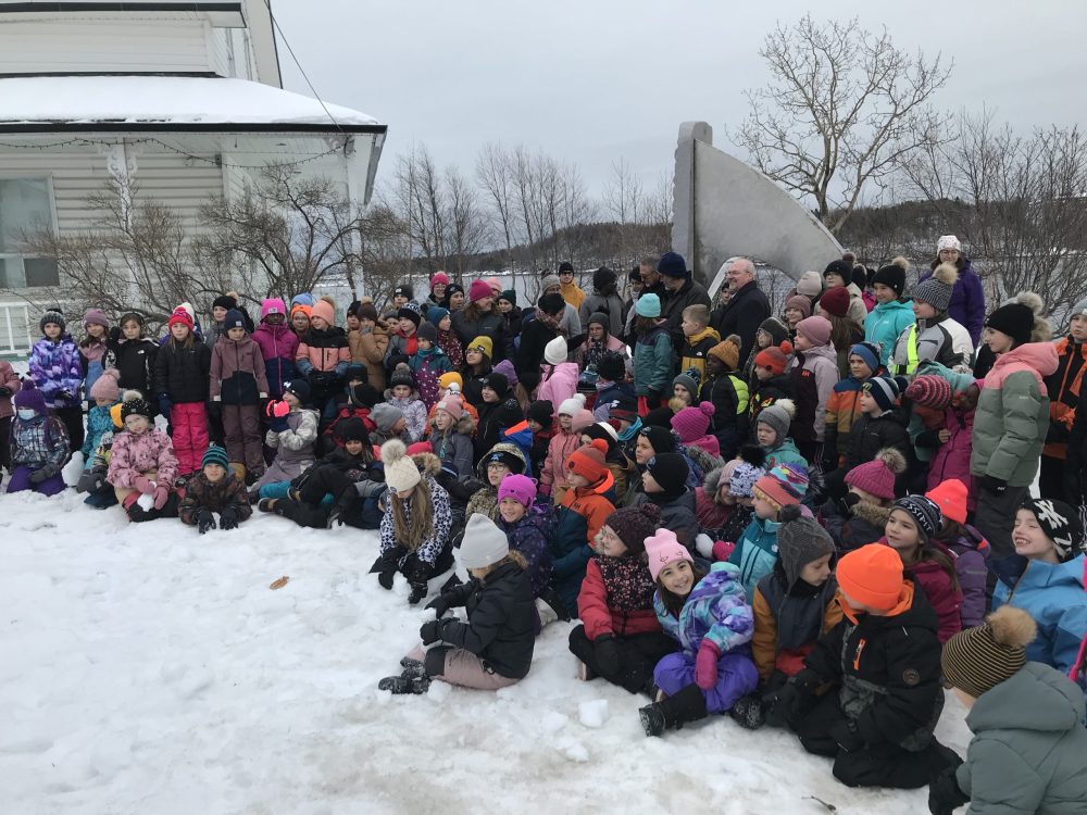 Plusieurs élèves habillées pour l'hiver à l'extérieur entourant la sculpture