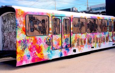 Wagon de train peinturé à l'aérosol avec des couleurs vives, des portraits de visage, et des structures de fer soudées ensemble qui représente d'autres dessins