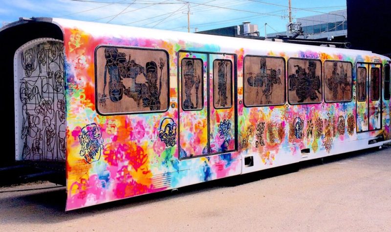 Wagon de train peinturé à l'aérosol avec des couleurs vives, des portraits de visage, et des structures de fer soudées ensemble qui représente d'autres dessins