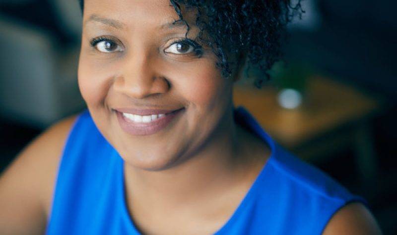 A smiling person in a blue shirt sitting down.