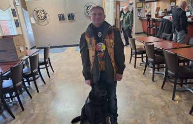 Indigenous Veteran Greg Janes stands proudly at the Royal Canadian Legion along with her service dog. Janes is also wearing an Iniigenous vest