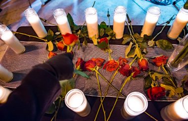 A circle of candles on the pavement with red roses in the centre of the circle.