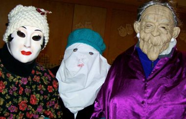 Trois personnes costumées avec masques, chapeaux et habits.