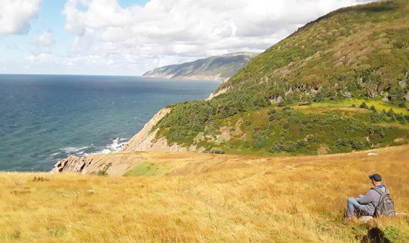 Un homme assis admirant les montagnes et la mer.