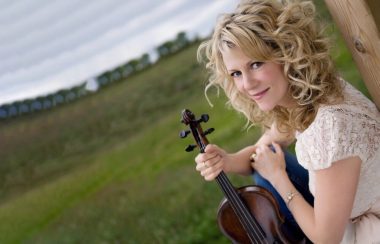 Une dame portant un chandail blanc tenant un violon.