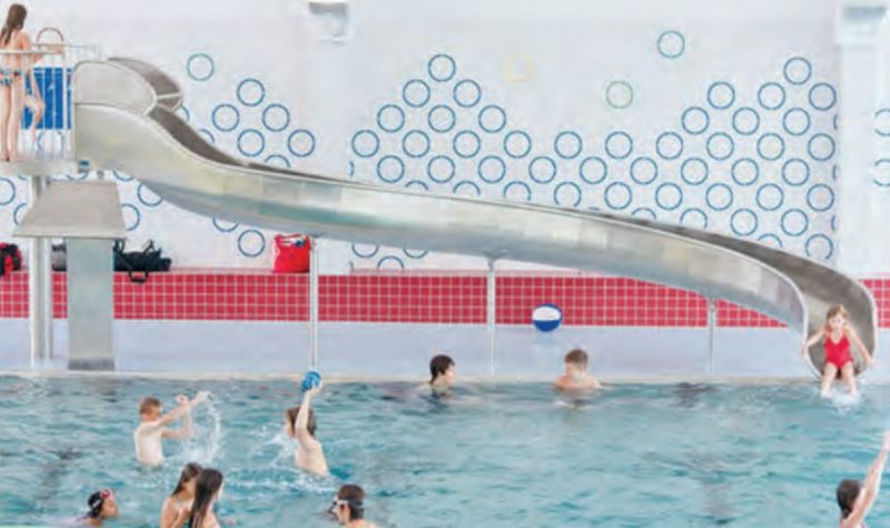 Des enfants jouent dans une piscine intérieure, avec une glissoire en arrière plan.