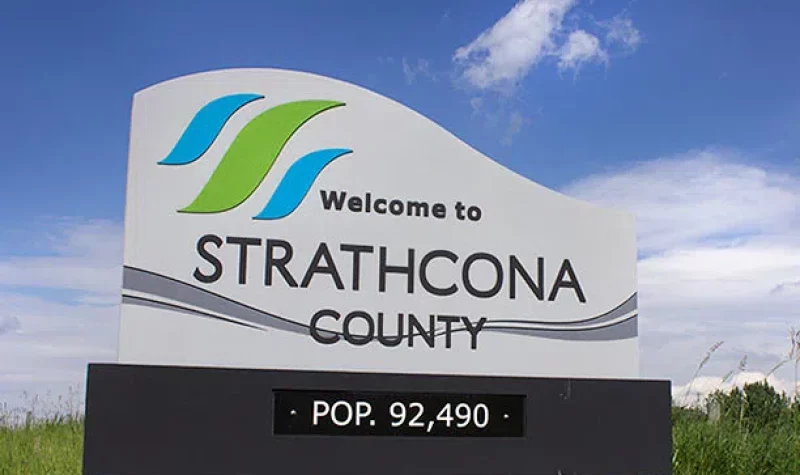 The welcome sign you see when coming into Strathcona County, with the logo on top, and the population on the bottom. Weather is partly cloudy.