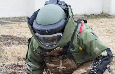 Une personne vêtu d'un uniforme de protection s'approche pour neutraiser une bombe dans un chant