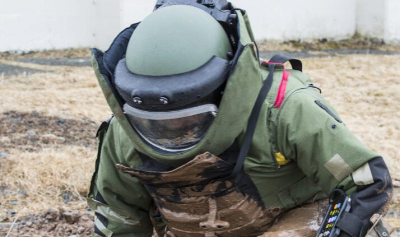 Une personne vêtu d'un uniforme de protection s'approche pour neutraiser une bombe dans un chant