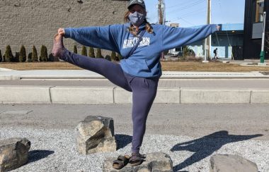 Cynthia Andal holding a yoga pose on a landscaping rock downtown.