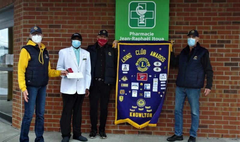 Three lions club members and local pharmacist. The lions club banner is k=held up between the people.