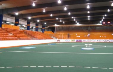 green turf floor inside an arena with orange seats in the distance.