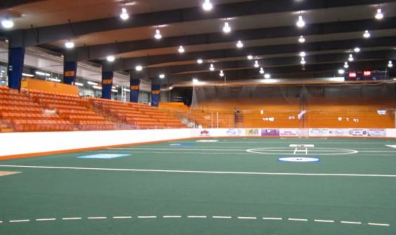 green turf floor inside an arena with orange seats in the distance.