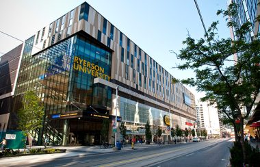 A brown and blue building with several glass windows and yellow text against a blue sky background on a street.