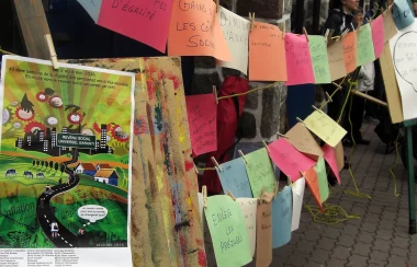 Handwritten signs clipped on a clothes line. Each sign highlights issues with poverty. There are also two multicoloured posters in the foreground..