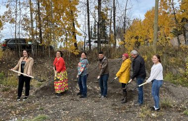 Seven people standing outside on a fall day, with shovels' holding dirt