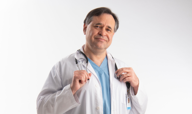 Dr Karl Weiss portant sarrau blanc, blouse bleue, stéthoscope au cou sur fond blanc