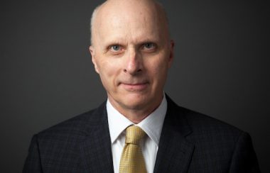 A man smiling, wearing a suit and tie