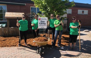 A group of people holding shovels with a barrel of mud. Behind the group is a sign for United Way's Day of Caring