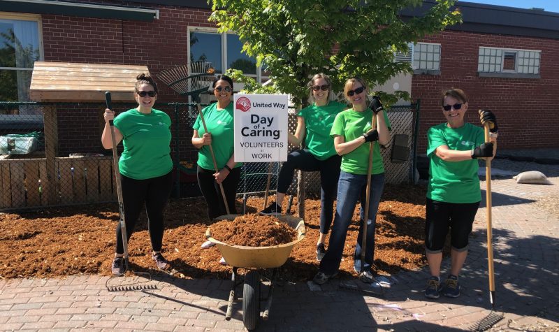 A group of people holding shovels with a barrel of mud. Behind the group is a sign for United Way's Day of Caring