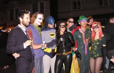 Several adults in batman themed costumes stand in a line.